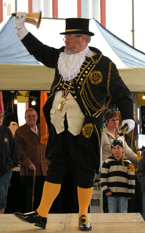 Town crier in black and gold rining a handbell
